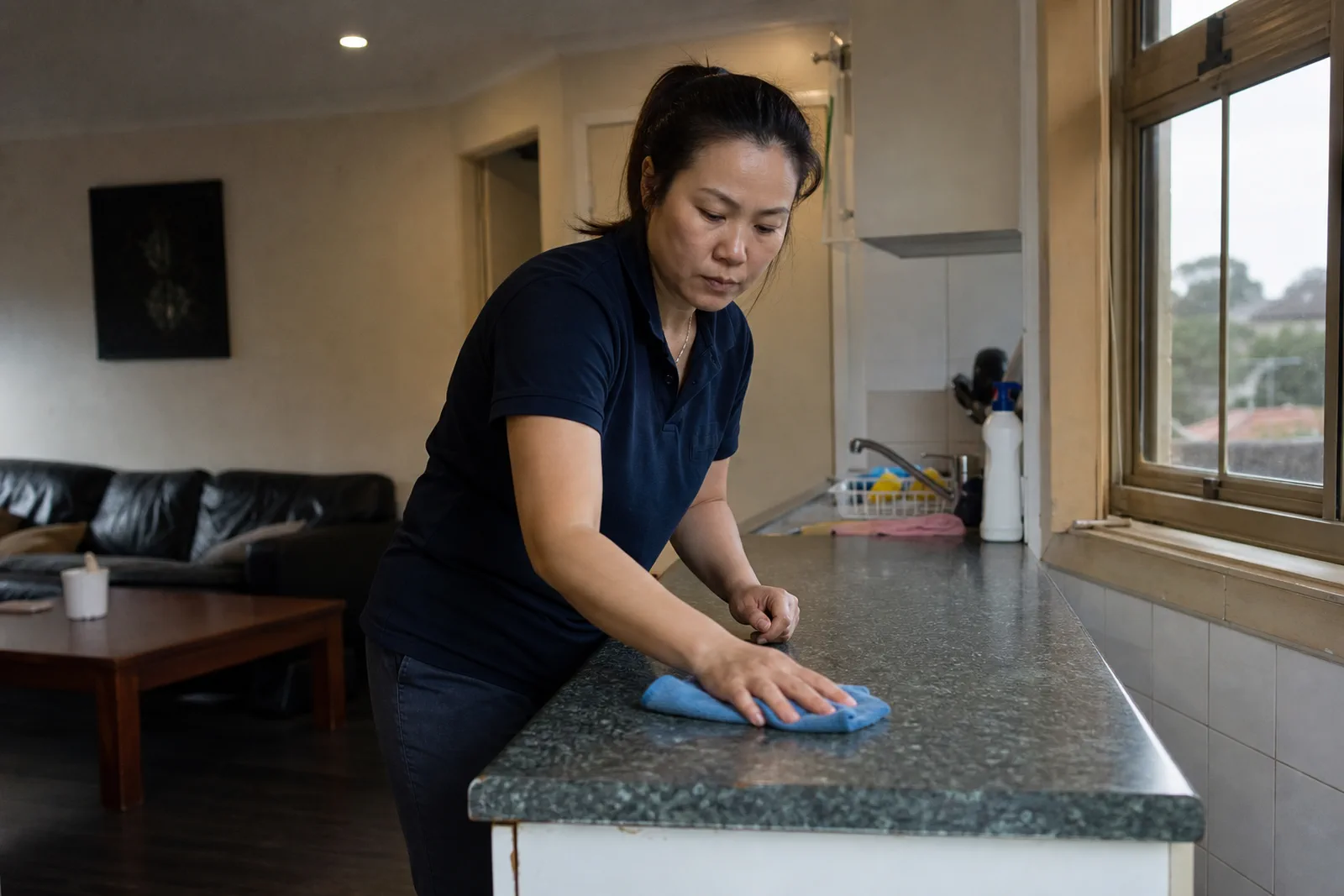 Cleaner wiping a kitchen bench in a compact lived-in home